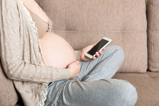 Valkoihoinen raskaana oleva tyttö käyttää kännykkää, lepää sängyssä kotona. - Valokuva, kuva