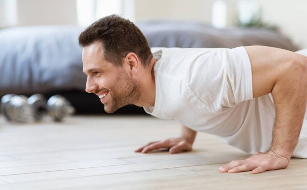 Sportovní muž dělá prkno cvičení na podlaze školení doma - Fotografie, Obrázek