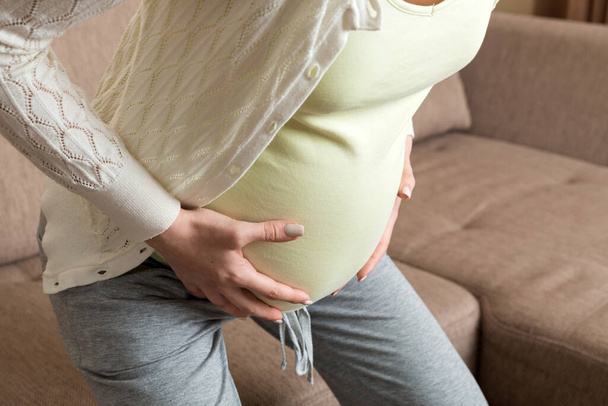 Mujer embarazada con el vientre doloroso en el sofá en casa. - Foto, imagen