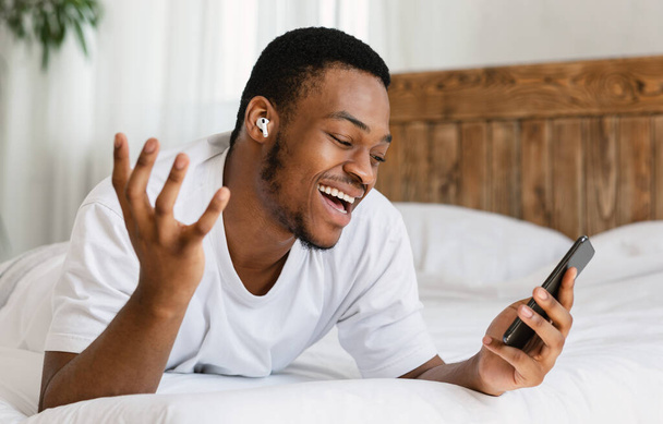 Schwarzer Mann mit Smartphone macht Videoanruf liegend im Bett - Foto, Bild