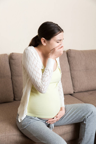 Embarazo por la mañana náuseas. Mujer embarazada teniendo náuseas sintiéndose mal en el sofá en el hogar. - Foto, imagen