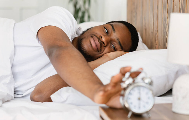 Dobrze spał czarny człowiek wyłączając budzik budząc się w sypialni - Zdjęcie, obraz