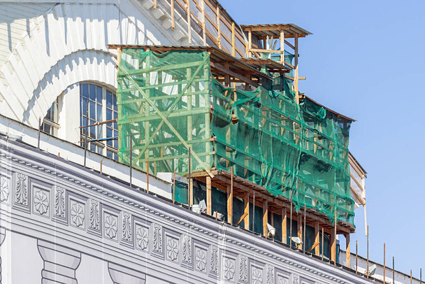 αποκατάσταση του κτιρίου και το ικρίωμα καλύπτεται με ένα πράσινο χρώμα πανί για την προστασία των ανθρώπων από τη σκόνη και τα συντρίμμια. το έργο των κατασκευαστών για τη διατήρηση των κτιρίων σε σωστή μορφή. - Φωτογραφία, εικόνα