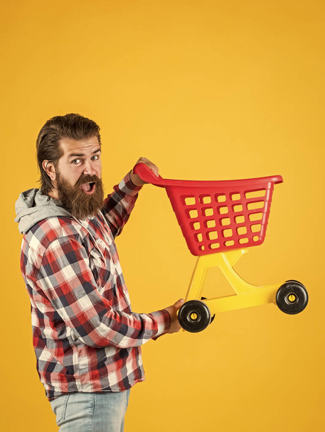 bearded man go shopping with toy empty shopping cart. customer pushing cart. buyer in supermarket. empty toy trolley. really busy housekeeper. perfect husband. need shopping list - Foto, imagen