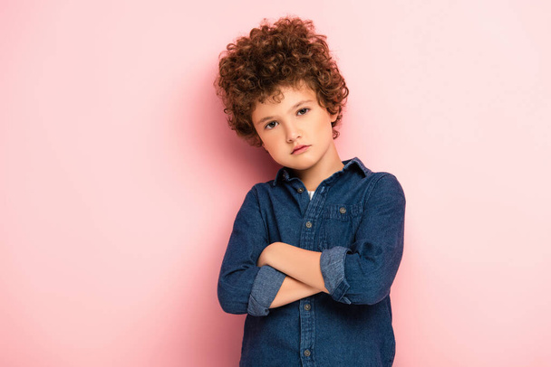serious and curly boy standing with crossed arms on pink  - Foto, immagini