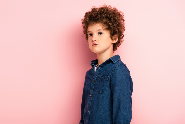 curly boy in denim shirt standing and looking away on pink  - Φωτογραφία, εικόνα