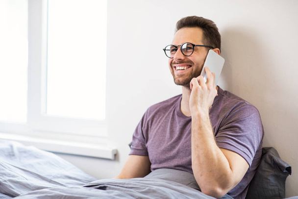 Guy Talking On Cellphone Sitting In Bed At Home - Φωτογραφία, εικόνα