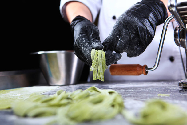 The chef rolls the pasta into nests. Homemade pasta. Dough with spinach. Health food. Unrecognizable person. Hands in protective gloves.Bottom view.Close up. - Foto, Bild