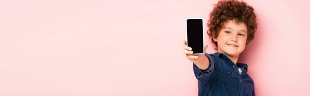 selective focus of curly boy in denim shirt holding smartphone with blank screen on pink, panoramic shot  - Zdjęcie, obraz