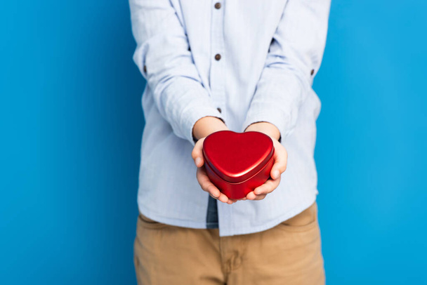 cropped view of boy holding red heart shape box on blue - Fotó, kép