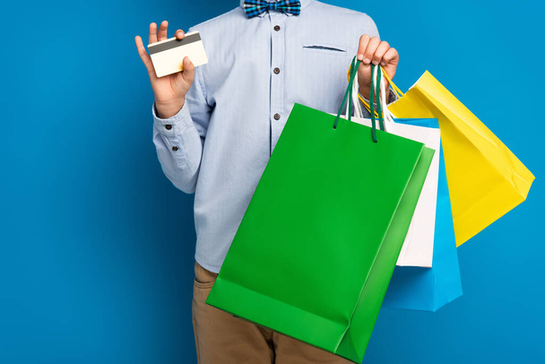 cropped view of boy holding shopping bags and credit card on blue  - Photo, Image