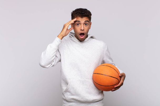 young man looking happy, astonished and surprised, smiling and realizing amazing and incredible good news. basket concept - Foto, imagen