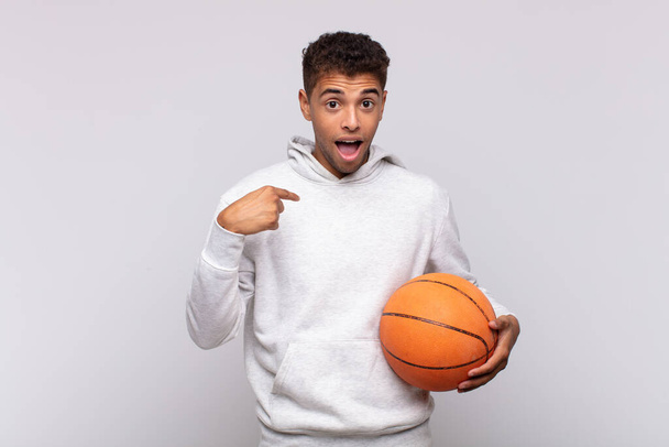young man feeling happy, surprised and proud, pointing to self with an excited, amazed look. basket concept - Фото, изображение