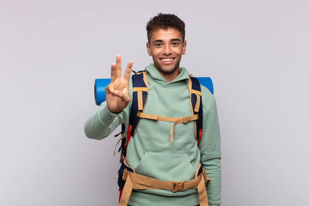 young hiker man smiling and looking friendly, showing number three or third with hand forward, counting down - Фото, изображение
