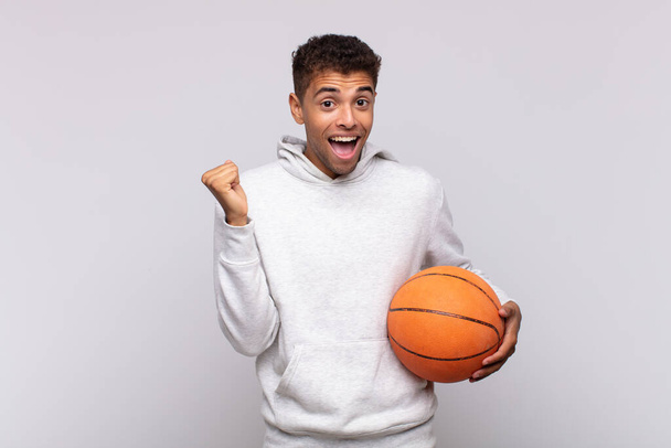 young man feeling shocked, excited and happy, laughing and celebrating success, saying wow!. basket concept - Foto, immagini