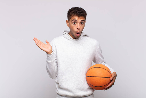 young man looking surprised and shocked, with jaw dropped holding an object with an open hand on the side. basket concept - 写真・画像
