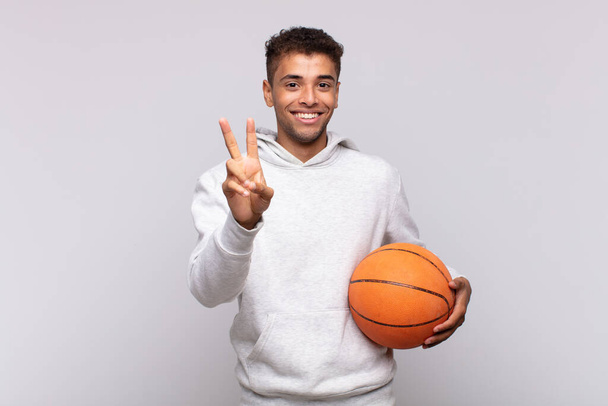 young man smiling and looking happy, carefree and positive, gesturing victory or peace with one hand. basket concept - Фото, изображение