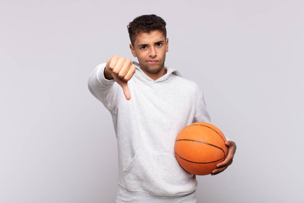 young man feeling cross, angry, annoyed, disappointed or displeased, showing thumbs down with a serious look. basket concept - Photo, Image
