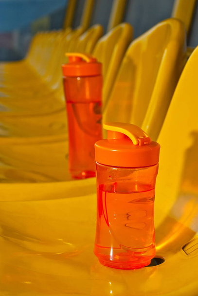 Na stadionu je spousta volných míst. Oranžová láhev s vodou na sedadle. Pij pro sportovce. Plastová sedadla jsou uspořádána v řadě. Špinavá a poškrábaná sedadla ventilátorů. - Fotografie, Obrázek