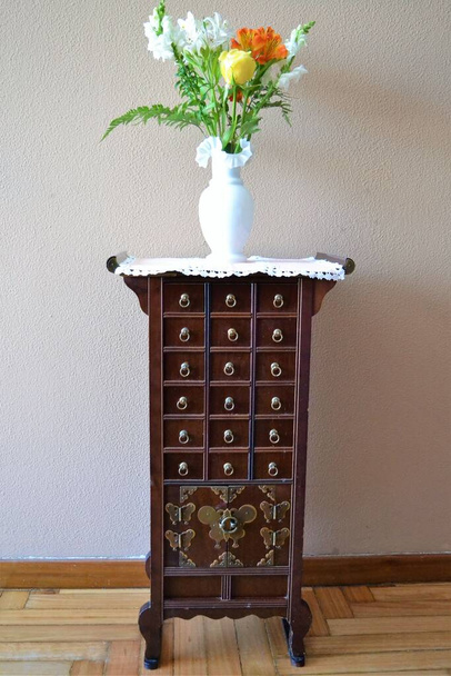 Китайский комод в гостиной с белой вазой наверху, содержащий букет цветов - Фото, изображение