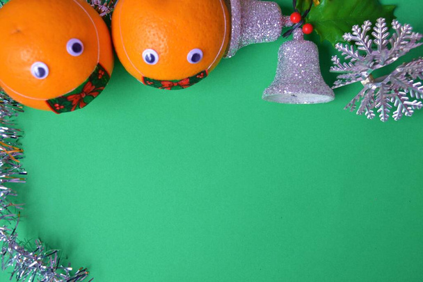 Yeşil arkaplanda, koronavirüsü önlemek için maske takmış iki portakaldan oluşan bir Noel çerçeve yapısı, iki çan, gümüş ve parlak bir yıldız, gümüş süs ve ökseotu. - Fotoğraf, Görsel