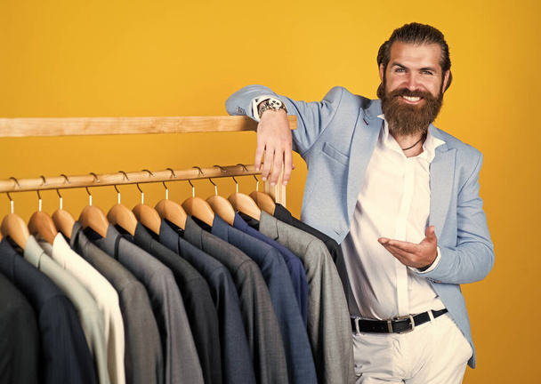 stylish mens clothing on hanger stand in room. business fashion style. dry cleaning service. style and people concept. Handsome man in smart casual wear looking at suits and choosing. Cool and sexy - Φωτογραφία, εικόνα