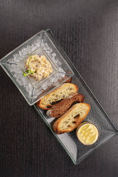 Pike fish caviar, on ice, with croutons and butter, on a transparent dish, on a dark background - Photo, Image