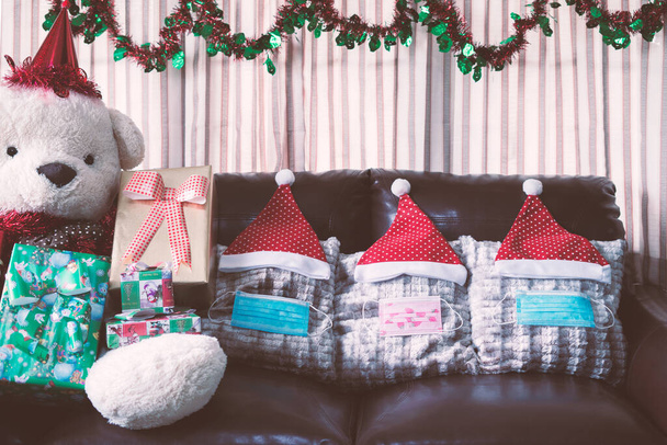 Noel süslemeleri ve üç tıbbi maske hediye kutusuyla şapkanın altında duruyor. - Fotoğraf, Görsel