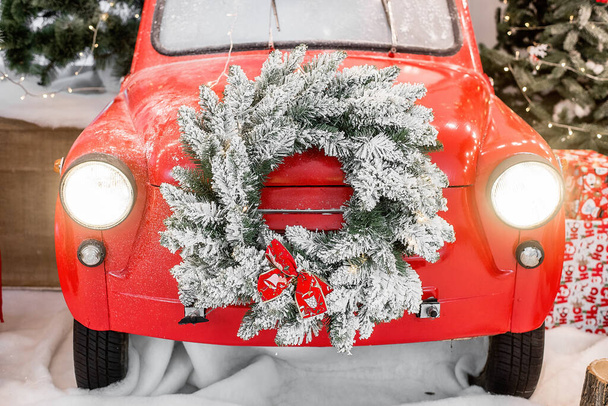 Magic card in red color. Decorated retro car with festive New Year lights, garlands, branches of Christmas trees, gift boxes in white-green wrapping paper, a wreath of pine needles. Copy space texture - Fotó, kép
