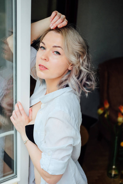 Een vrouw in haar flat kleedt zich aan bij het raam. Franse stijl. Moderne kleurrijke kapsel. - Foto, afbeelding