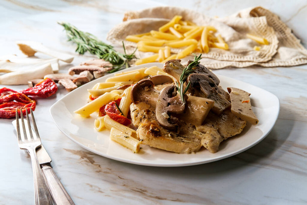 Κρεμώδης ιταλική μαρσάλα κοτόπουλου με μανιτάρια στρειδιών King και λιαστές ντομάτες που σερβίρονται πάνω από πένες rigate ζυμαρικά - Φωτογραφία, εικόνα