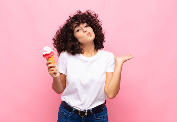 young woman with an ice cream feeling puzzled and confused, doubting, weighting or choosing different options with funny expression - Zdjęcie, obraz
