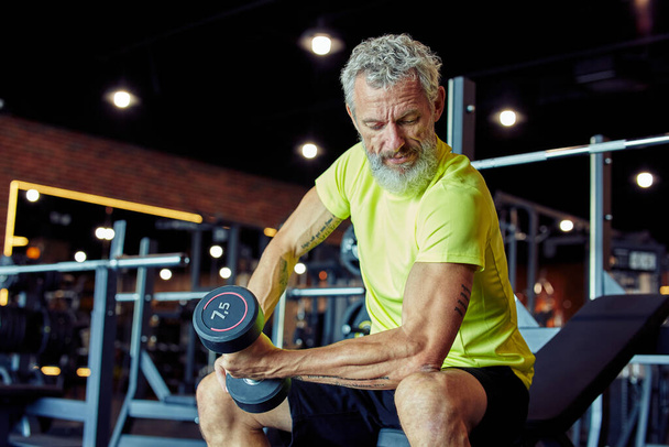 Cvičení na váhu. Soustředěný dospělý muž ve sportovním oblečení zvedání těžké činky a čerpání jeho biceps při tréninku v posilovně - Fotografie, Obrázek