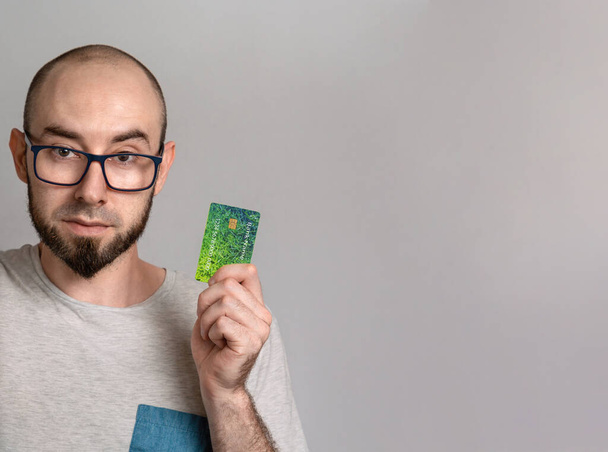 Bankacılık ve kredi kartı harcamaları kavramı. Gözlüklü bir adam gülümsüyor ve elinde bir banka kartı tutuyor. Kapat ve boşluğu kopyala. - Fotoğraf, Görsel