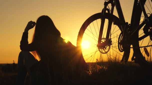 Das Mädchen ist bei Sonnenuntergang mit dem Fahrrad unterwegs. Alleingang während einer Pandemie. Abenteuer und Reisekonzept. Gesunde junge Wanderin sitzt auf dem Hügel neben dem Fahrrad und genießt die Natur und die Sonne - Filmmaterial, Video