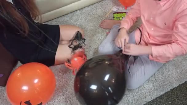Chica sosteniendo una guirnalda de papel con arañas para decorar la casa, un niño atando un globo. Los niños se preparan para celebrar Halloween en casa - Imágenes, Vídeo