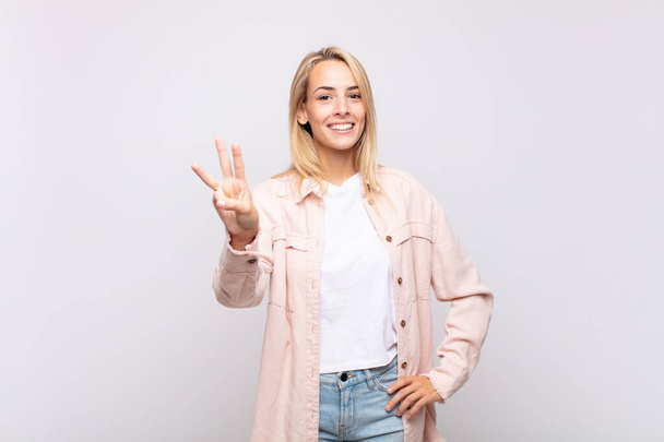 Woman smiling and looking friendly, showing number three or third with hand forward, counting down - Foto, afbeelding