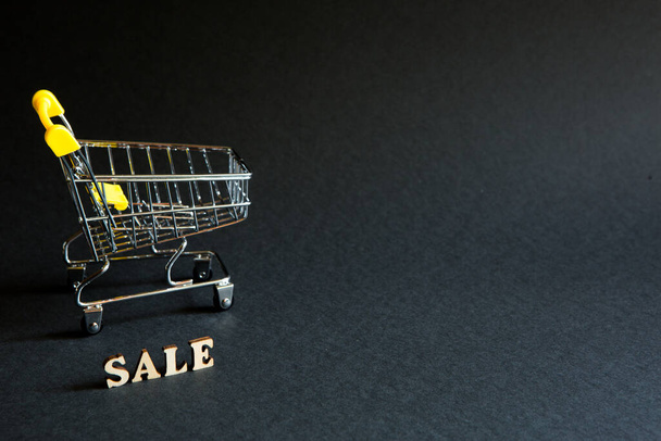 Shopping cart and the inscription "Sale" on a black background. Black Friday, discounts, sale, shopping, interest sign. Space for text - Φωτογραφία, εικόνα