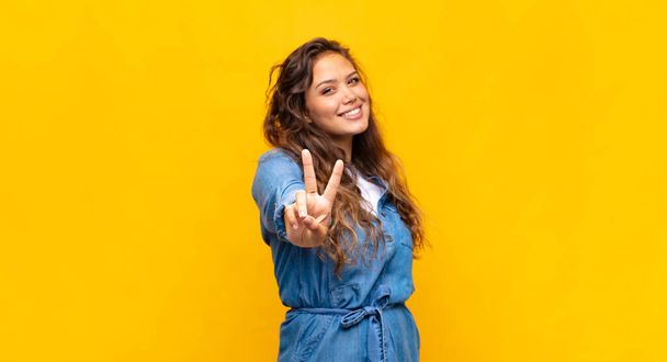 Girl smiling and looking happy, carefree and positive, gesturing victory or peace with one hand - Foto, afbeelding