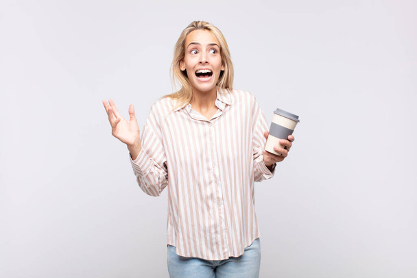 young woman with a coffee feeling happy, excited, surprised or shocked, smiling and astonished at something unbelievable - Photo, Image