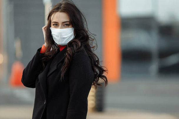 Πορτρέτο της όμορφης γυναίκας που περπατά στο δρόμο φορώντας προστατευτική μάσκα ως προστασία από μολυσματικές ασθένειες. Ελκυστικό δυστυχισμένο μοντέλο με γρίπη σε εξωτερικούς χώρους. - Φωτογραφία, εικόνα