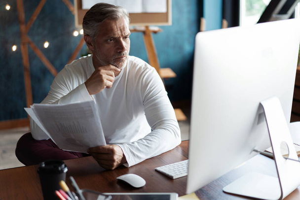 Casual Grey-haired businessman looking through paper documents. Male accounting manager reviewing financial report - Foto, imagen