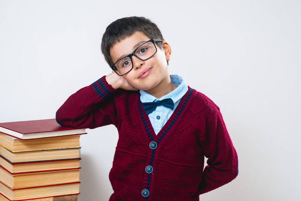 L'écolier avec des lunettes et un pull rouge se tient avec sa main sur une pile de livres. - Photo, image