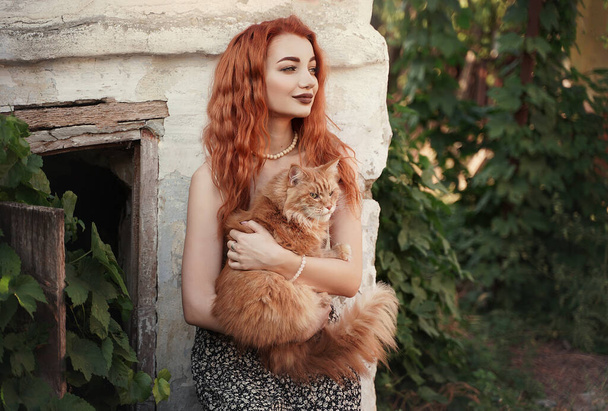 Red-haired girl with a red cat in the countryside. - Foto, imagen