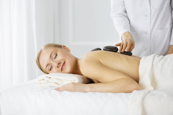 Beautiful caucasian woman enjoying warm stones procedure with closed eyes. Beauty and Spa salon concept - Foto, afbeelding
