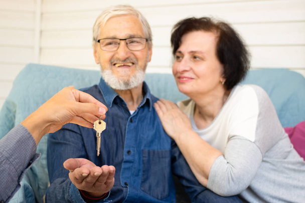 Aufgeregt lächelndes älteres Familienpaar, das nach der Unterzeichnung des Kaufvertrages beim Treffen mit dem Makler den Schlüssel zum eigenen Haus bekommt. Glückliches und wohlhabendes Alterskonzept. Selektiver Fokus - Foto, Bild