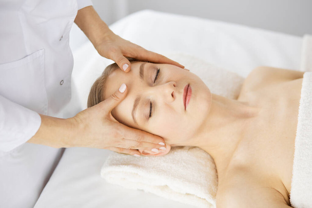 Beautiful caucasian woman enjoying facial massage with closed eyes in spa salon. Relaxing treatment in medicine and Beauty concept - Foto, imagen