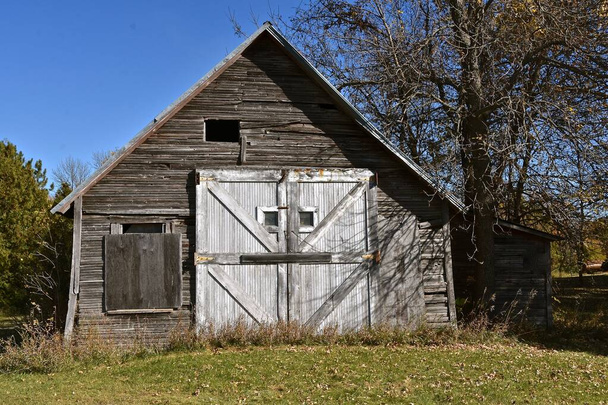 Stará vratká kůlna s několika odstíny ošlehaného dřeva a zabedněným oknem na opuštěné farmě. - Fotografie, Obrázek