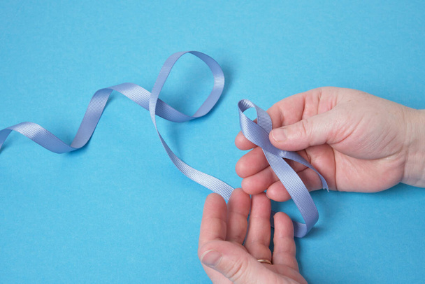 grandmother and granddaughter hold a blue ribbon on a blue background, child's hands and woman's hands, copy space , diabetes and cancer symbol - Photo, Image