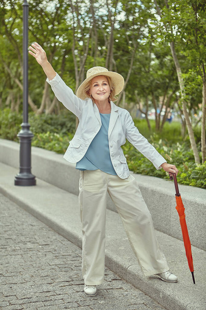 Smiling mature European woman waving to someone in a public park. - Zdjęcie, obraz